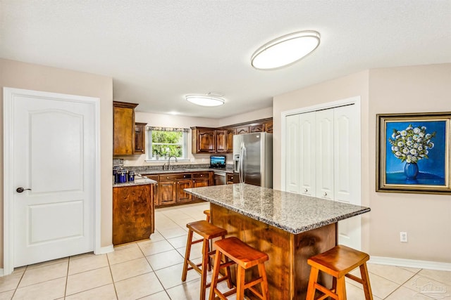 kitchen featuring stainless steel appliances, light stone countertops, sink, a breakfast bar area, and a center island