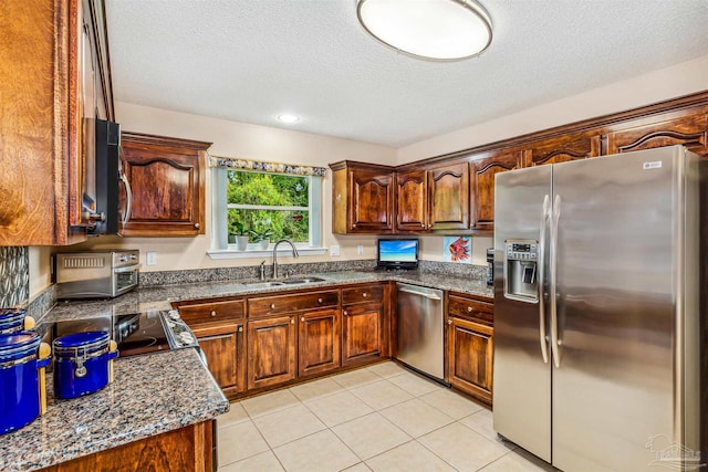 kitchen featuring appliances with stainless steel finishes, sink, dark stone countertops, and light tile patterned floors