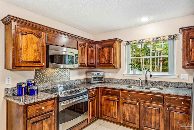 kitchen featuring sink, appliances with stainless steel finishes, dark stone countertops, a textured ceiling, and light tile patterned floors