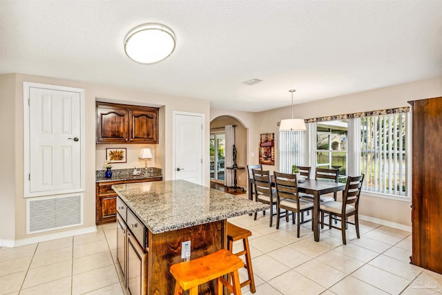 kitchen featuring light stone counters, a center island, a textured ceiling, light tile patterned floors, and pendant lighting