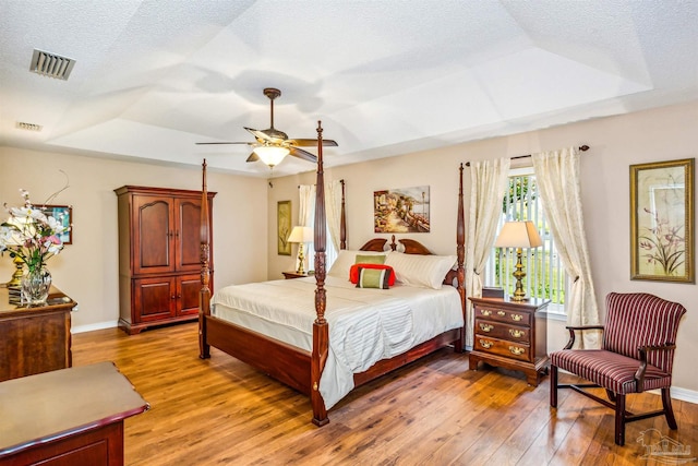 bedroom with a textured ceiling, hardwood / wood-style flooring, ceiling fan, and a tray ceiling