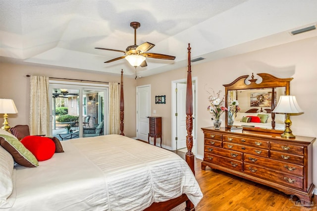 bedroom featuring a textured ceiling, a raised ceiling, access to exterior, hardwood / wood-style flooring, and ceiling fan