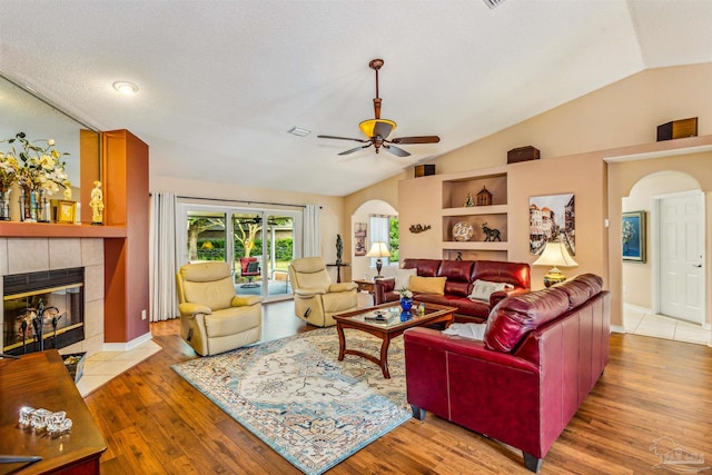 living room featuring light hardwood / wood-style floors, lofted ceiling, a textured ceiling, ceiling fan, and a fireplace