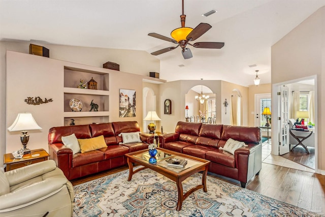 living room featuring built in shelves, ceiling fan with notable chandelier, hardwood / wood-style flooring, and vaulted ceiling