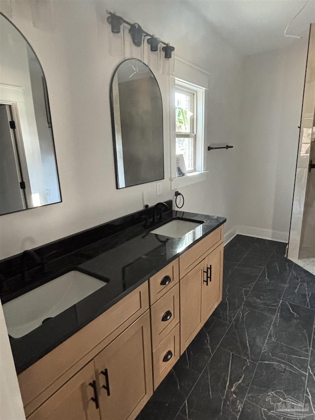 full bath featuring marble finish floor, double vanity, a sink, and baseboards