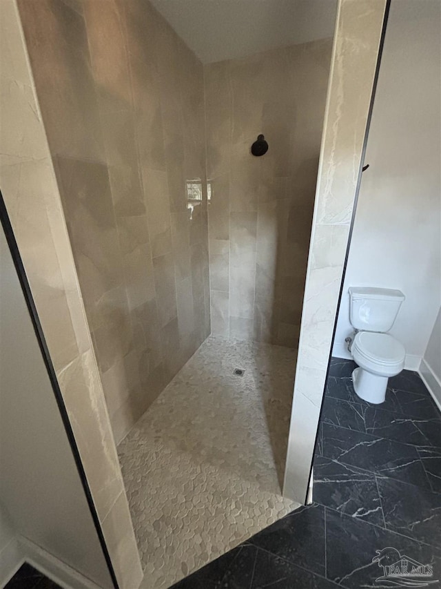 full bath featuring marble finish floor, tiled shower, toilet, and baseboards