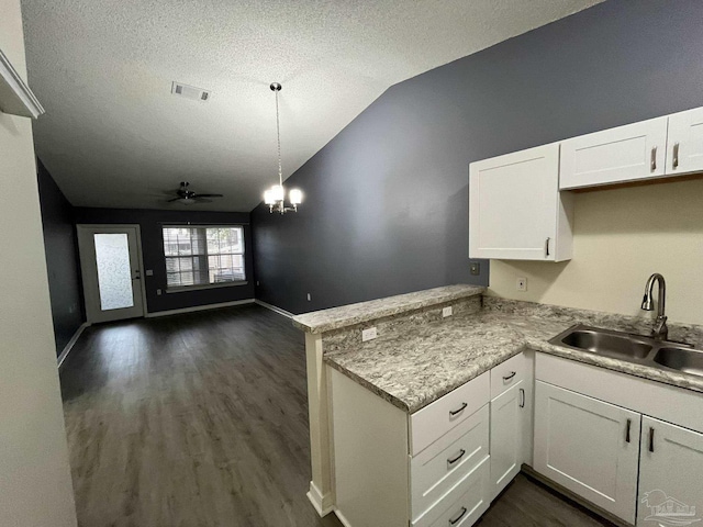 kitchen featuring lofted ceiling, a peninsula, a sink, visible vents, and white cabinets