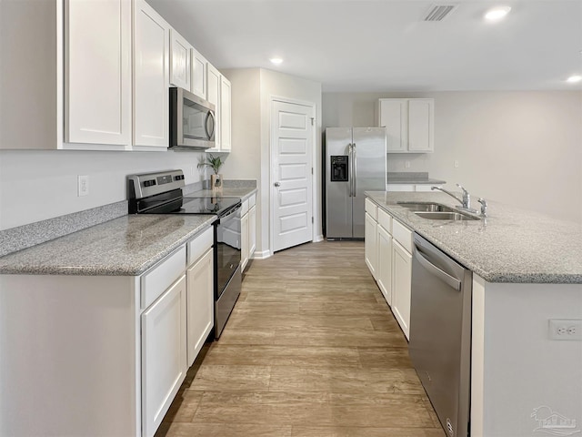 kitchen with visible vents, a center island with sink, a sink, stainless steel appliances, and light wood-style floors