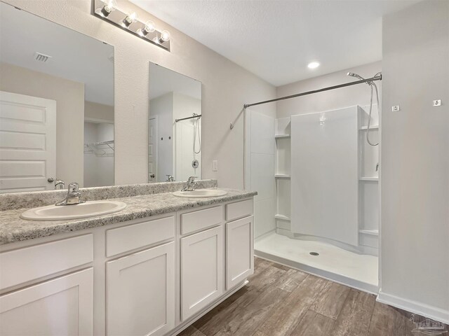 bathroom featuring walk in shower, wood finished floors, visible vents, and a sink