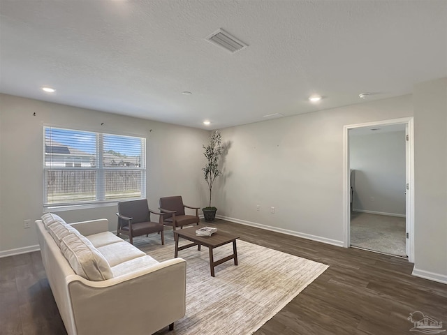 living area with visible vents, baseboards, a textured ceiling, and wood finished floors