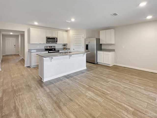 kitchen featuring light wood finished floors, visible vents, a kitchen breakfast bar, stainless steel appliances, and white cabinetry