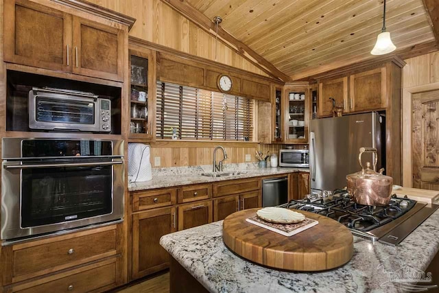 kitchen featuring light stone countertops, stainless steel appliances, wooden walls, and sink