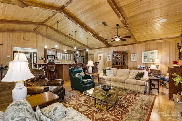 living room with wood walls, wooden ceiling, vaulted ceiling with beams, ceiling fan, and light wood-type flooring