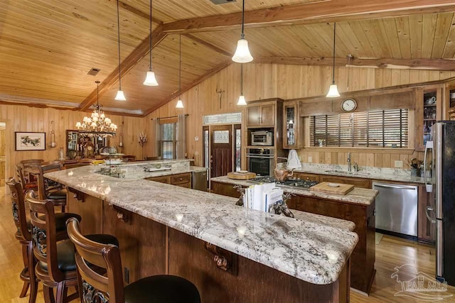 kitchen with hanging light fixtures, built in appliances, vaulted ceiling with beams, hardwood / wood-style flooring, and light stone counters