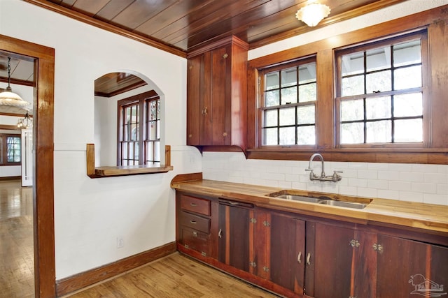 kitchen with light wood finished floors, butcher block counters, crown molding, and a sink