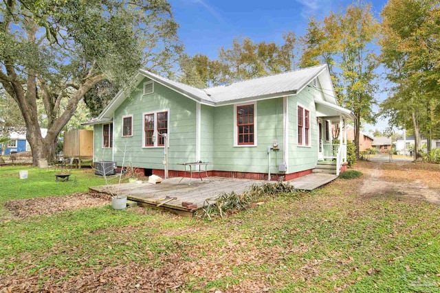 back of house with metal roof, central AC, and a lawn