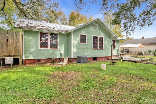 back of property with fence, metal roof, central AC, and a yard