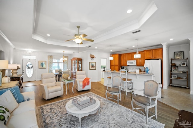 living room featuring ceiling fan with notable chandelier, light hardwood / wood-style flooring, crown molding, and a tray ceiling