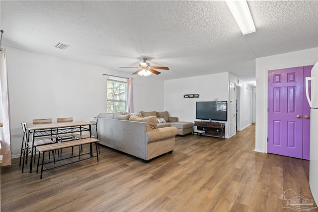 living area with a textured ceiling, ceiling fan, wood finished floors, and visible vents