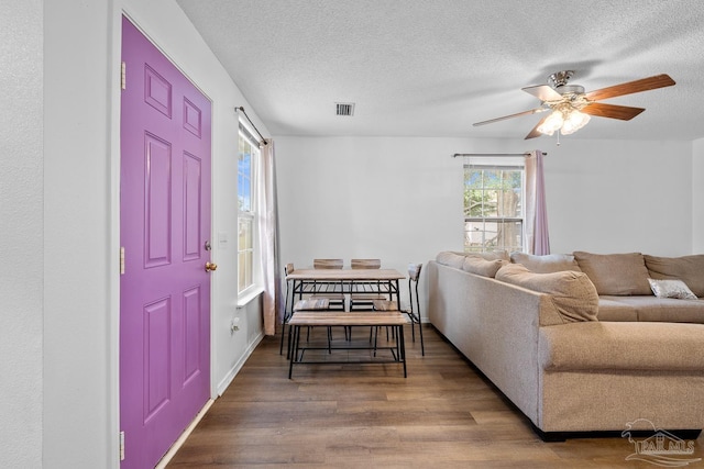 living room featuring ceiling fan, a textured ceiling, visible vents, and wood finished floors