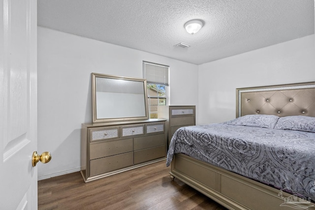 bedroom featuring visible vents, a textured ceiling, baseboards, and wood finished floors