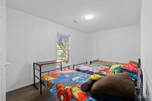 bedroom featuring visible vents, a textured ceiling, baseboards, and wood finished floors