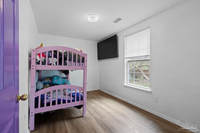 bedroom featuring baseboards, a textured ceiling, visible vents, and wood finished floors