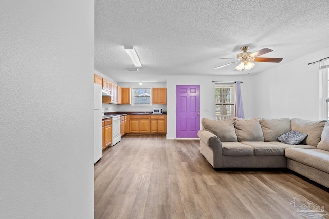 unfurnished living room with a textured ceiling, a sink, light wood-style flooring, and a ceiling fan