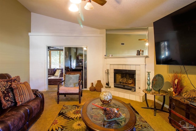 carpeted living room with ceiling fan, lofted ceiling, a tiled fireplace, and a textured ceiling