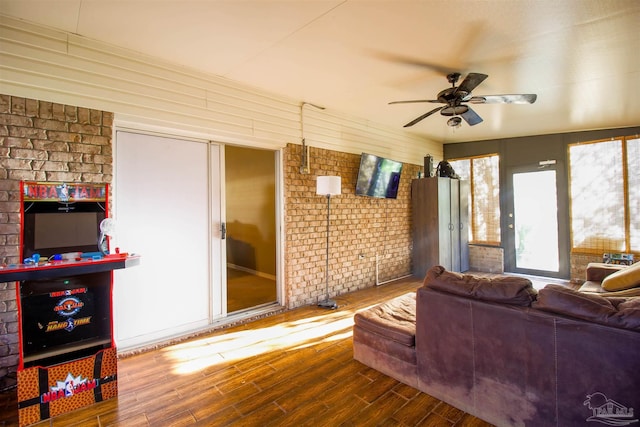 living room featuring wood-type flooring, brick wall, and ceiling fan