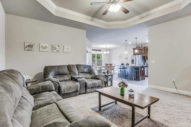 carpeted living room featuring a tray ceiling, ceiling fan with notable chandelier, and ornamental molding