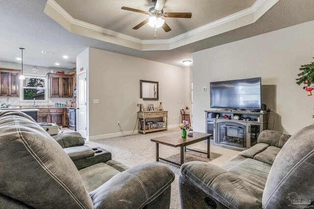 carpeted living room with ceiling fan, ornamental molding, a fireplace, and a tray ceiling