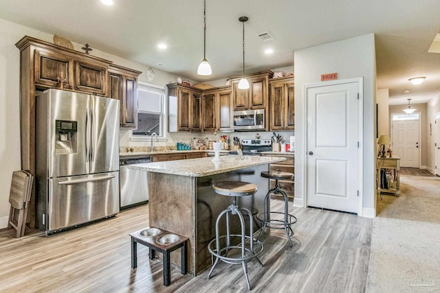 kitchen with light stone countertops, appliances with stainless steel finishes, sink, decorative light fixtures, and a center island