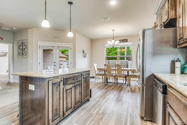 kitchen with an inviting chandelier, stainless steel dishwasher, decorative light fixtures, a kitchen island, and light stone counters