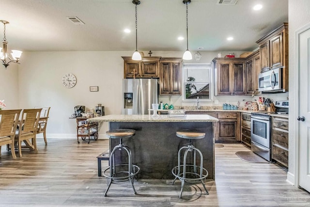 kitchen with pendant lighting, light hardwood / wood-style flooring, appliances with stainless steel finishes, a kitchen island, and a chandelier