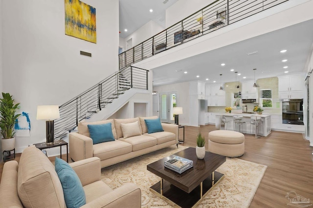 living room featuring light wood finished floors, recessed lighting, visible vents, a towering ceiling, and stairs