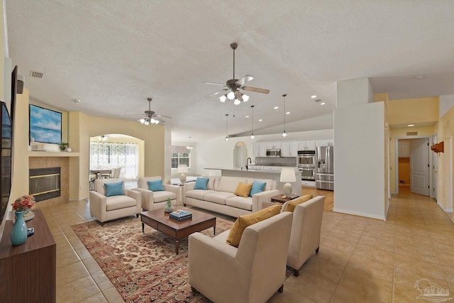 tiled living room featuring a tile fireplace, sink, vaulted ceiling, ceiling fan, and a textured ceiling