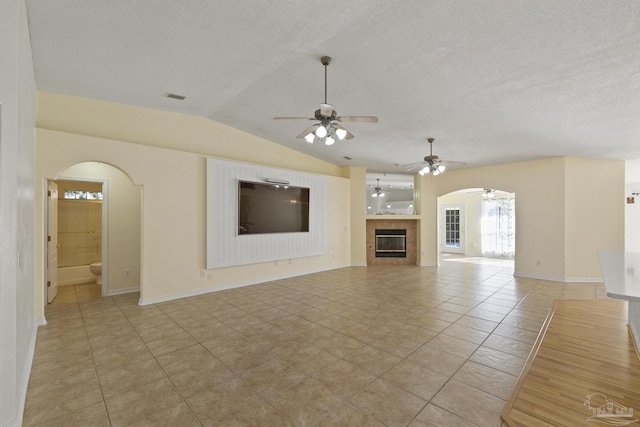 unfurnished living room featuring lofted ceiling, a tile fireplace, ceiling fan, a textured ceiling, and light tile patterned flooring