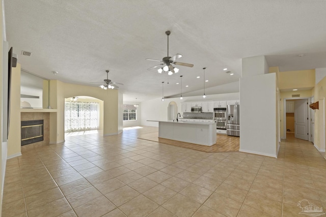 unfurnished living room with a tile fireplace, sink, ceiling fan, light tile patterned floors, and a textured ceiling