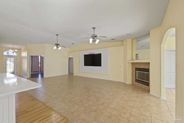 unfurnished living room with a tile fireplace, lofted ceiling, light tile patterned floors, and ceiling fan with notable chandelier