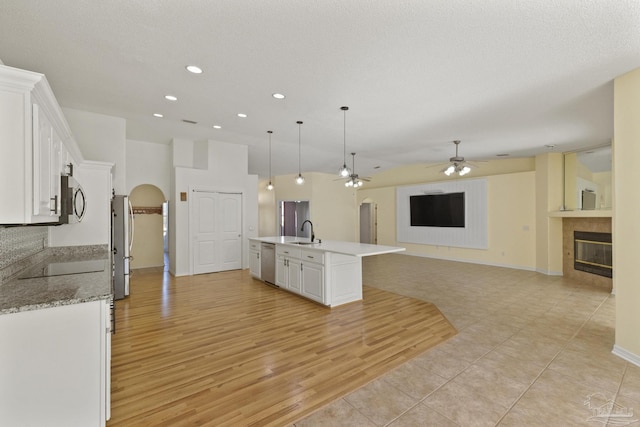 kitchen with white cabinets, hanging light fixtures, light wood-type flooring, an island with sink, and appliances with stainless steel finishes