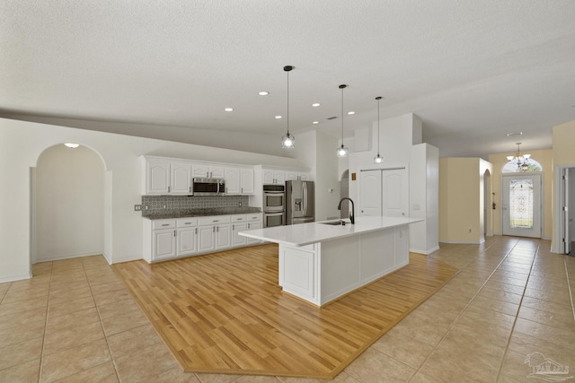 kitchen with white cabinets, decorative light fixtures, a kitchen island with sink, and appliances with stainless steel finishes