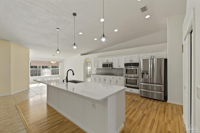 kitchen with hanging light fixtures, vaulted ceiling, light wood-type flooring, white cabinetry, and stainless steel appliances