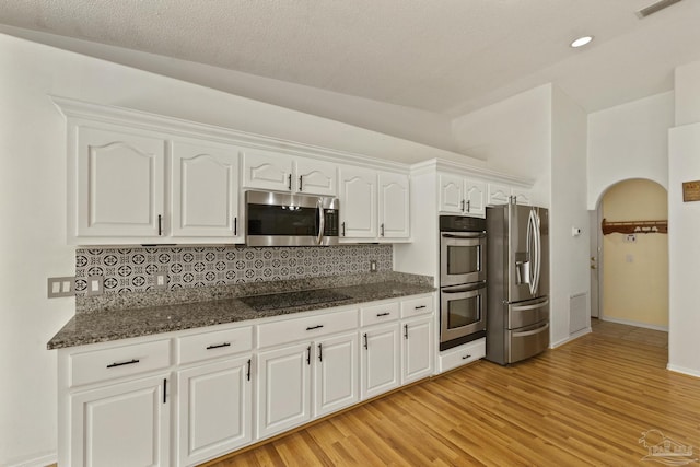 kitchen featuring backsplash, dark stone countertops, light hardwood / wood-style floors, white cabinetry, and stainless steel appliances