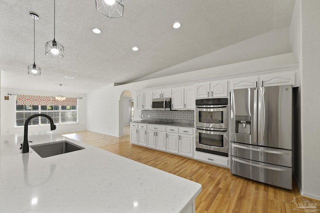 kitchen with decorative light fixtures, white cabinetry, appliances with stainless steel finishes, and vaulted ceiling