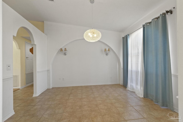 tiled spare room featuring an inviting chandelier