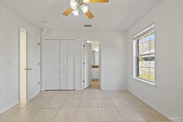 unfurnished bedroom with ensuite bath, a textured ceiling, ceiling fan, a closet, and light tile patterned flooring