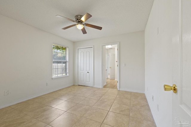 unfurnished bedroom featuring ceiling fan, a closet, light tile patterned floors, and a textured ceiling