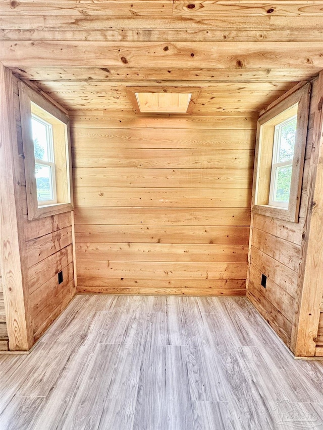 unfurnished room with a healthy amount of sunlight, light wood-type flooring, and wooden walls