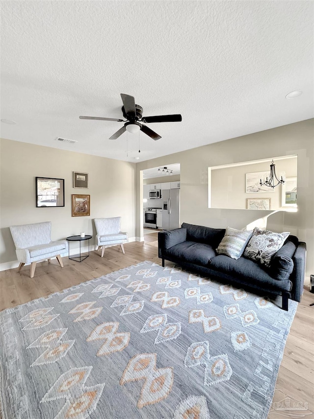 living room featuring a textured ceiling, ceiling fan with notable chandelier, and light wood-type flooring